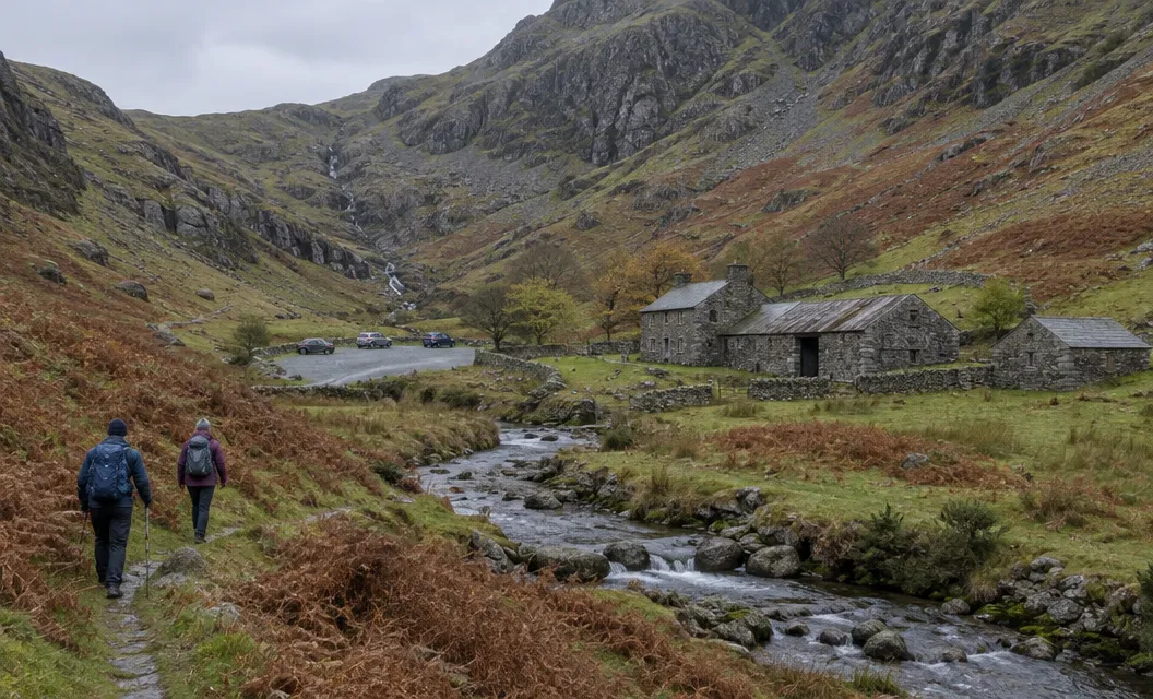 A narrow valley with a stream and a few stone farm buildings below steep crags.