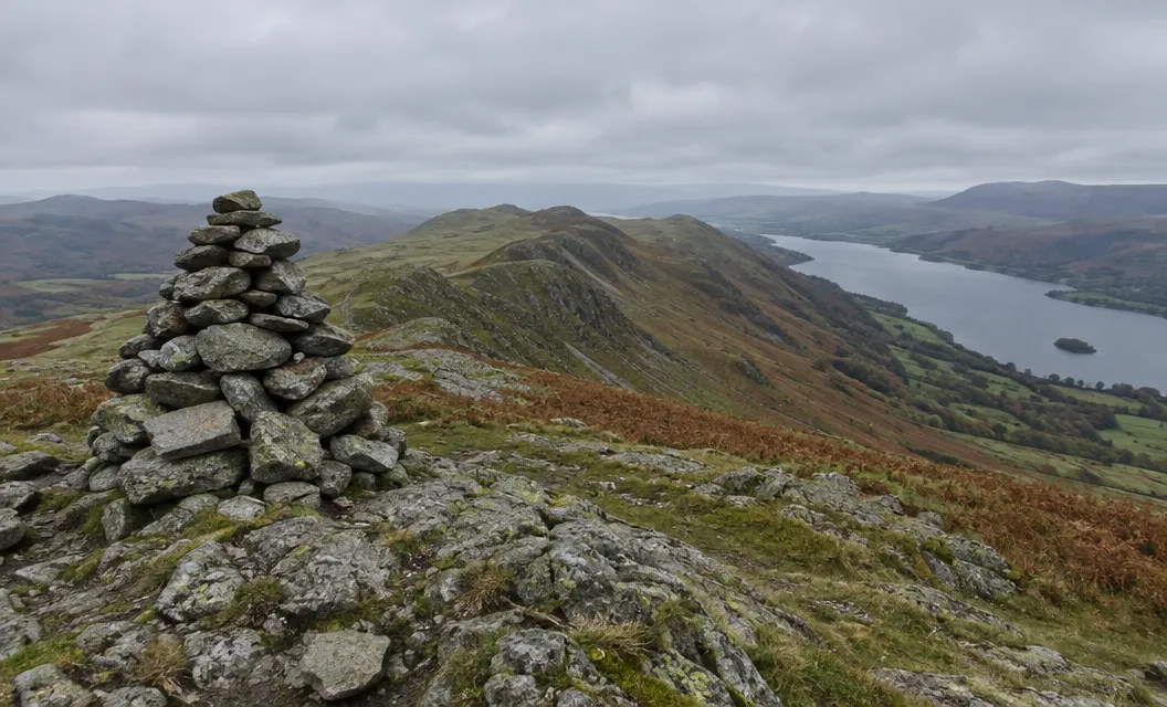 A large stone cairn on a rocky summit, a ridge dropping away towards a lake.