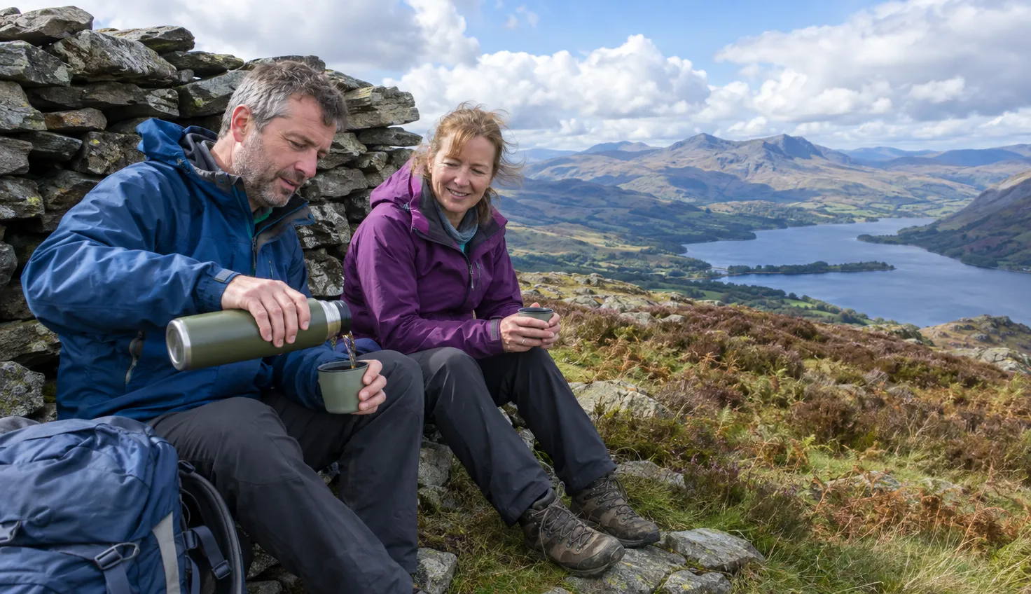 Two walkers resting at the stone shelter on the summit of Arenig Fawr with a wide view west
