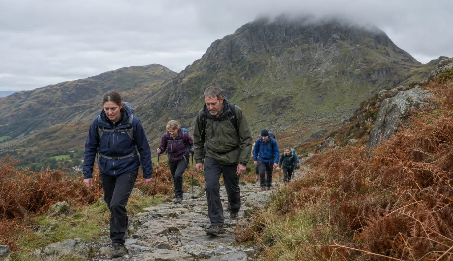 A group of walkers climbing a broad stone path towards a summit with cloud on its top.