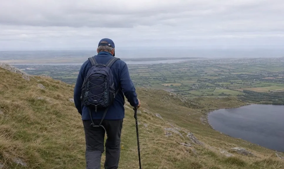 A walker climbing a broad grassy mountain shoulder with a valley behind