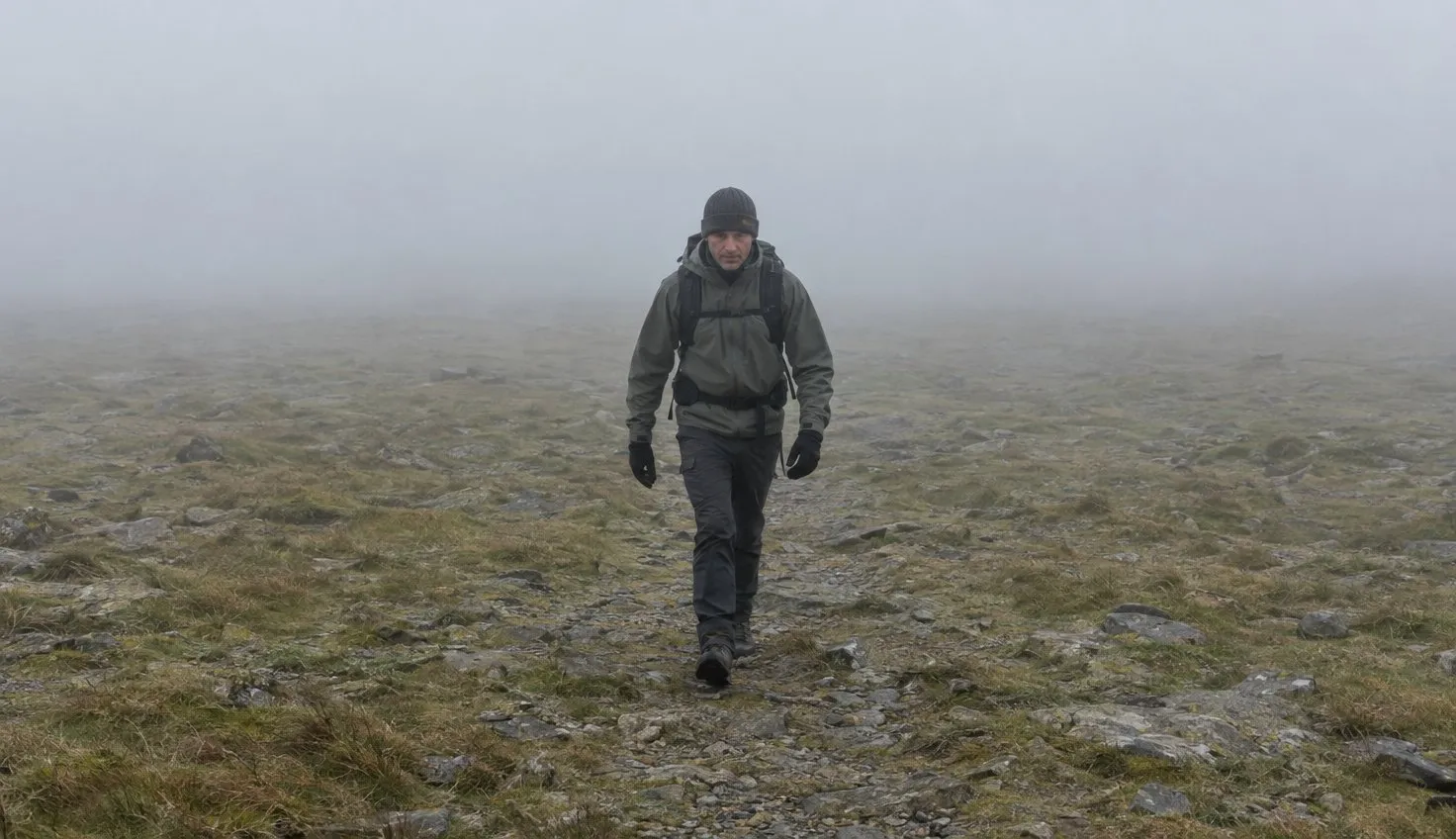 A walker crossing a broad, bare stony mountain plateau with mist fading the ground out on every side.