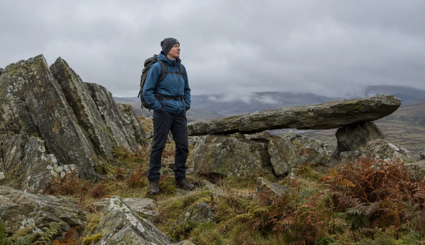 A walker among leaning slabs and boulders on a rocky summit plateau, beside a long flat slab balanced on rocks.