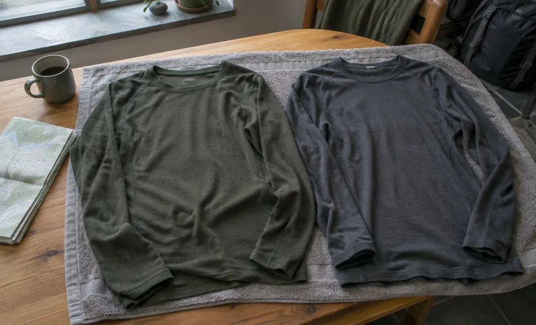 Two long-sleeved base layer tops laid flat on a towel to dry indoors.