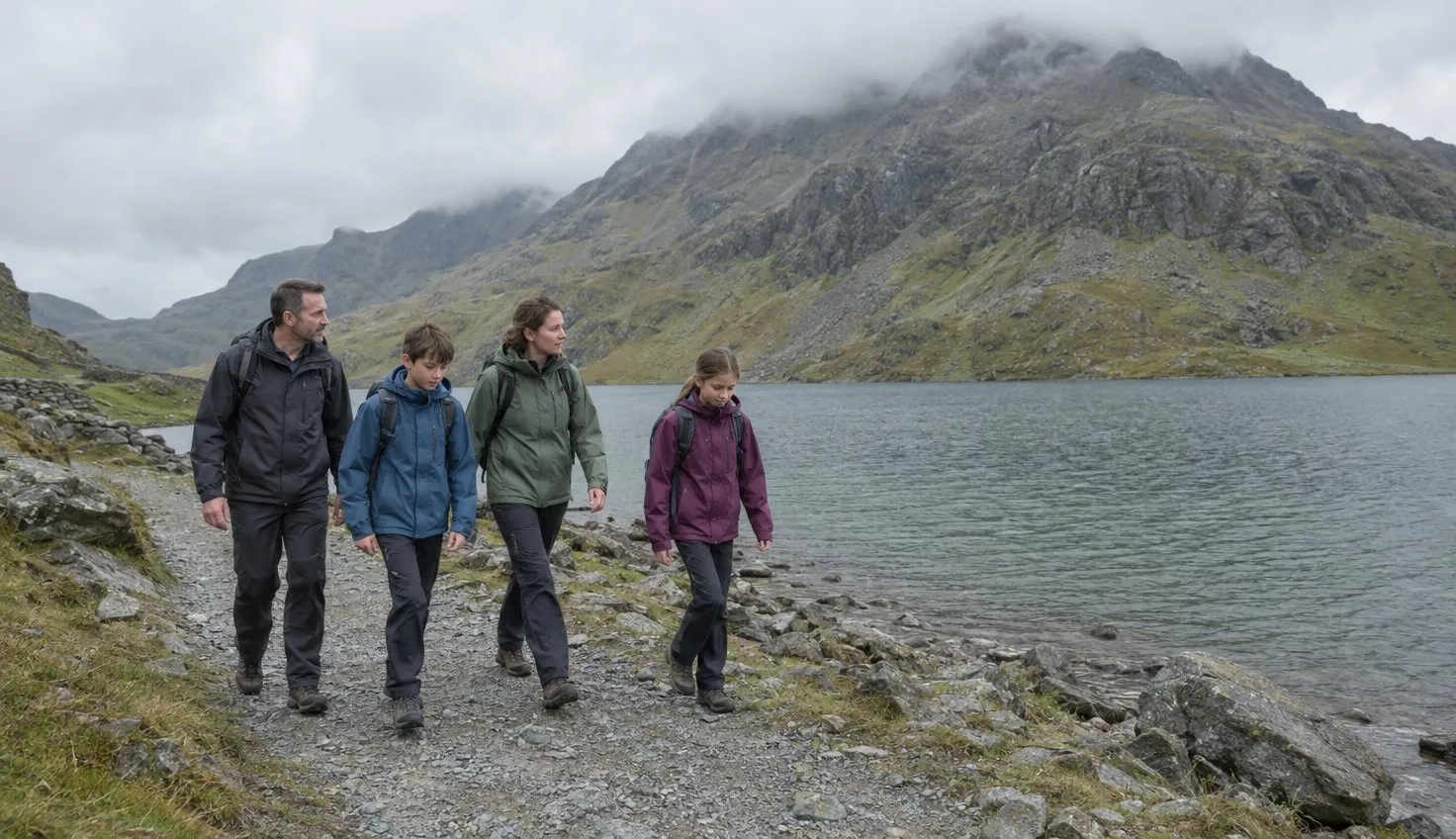 A family walking a wide flat stony track along the shore of a large mountain lake, steep peaks rising behind.