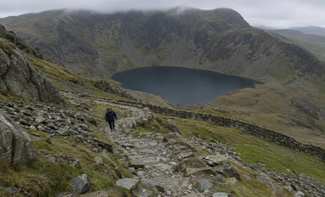 A steep rocky path zigzagging up loose ground above a dark lake in a deep corrie.