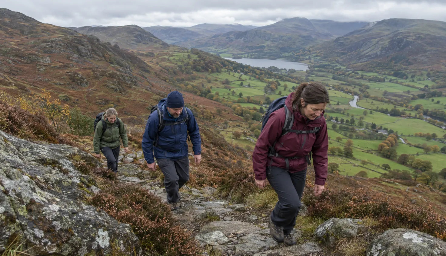 Three walkers climbing rocky steps on a steep mountain slope.