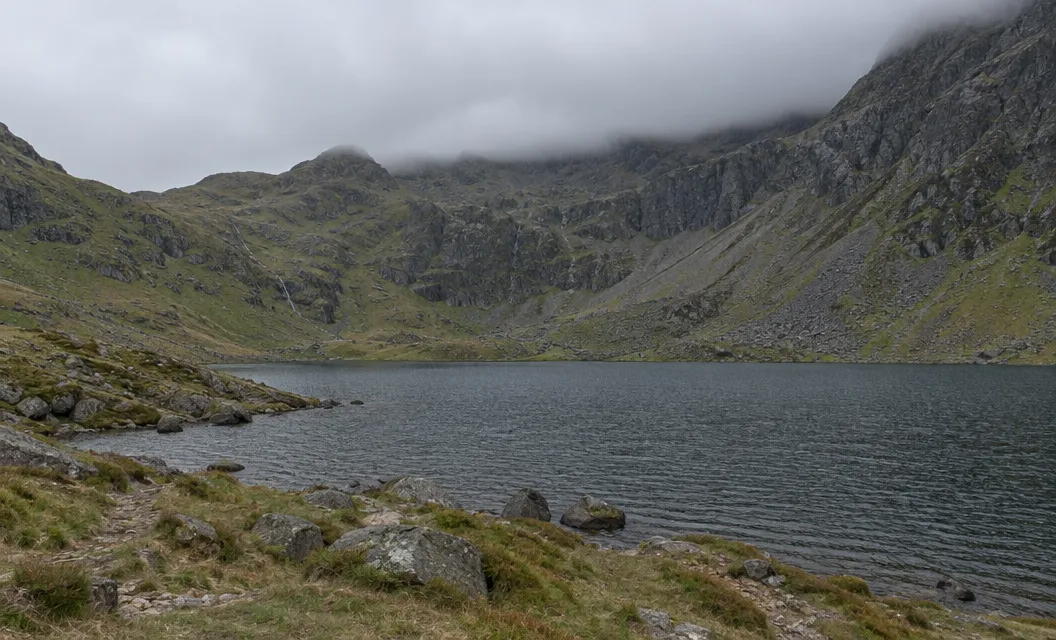 A mountain corrie lake beneath steep rocky slopes and low grey cloud.