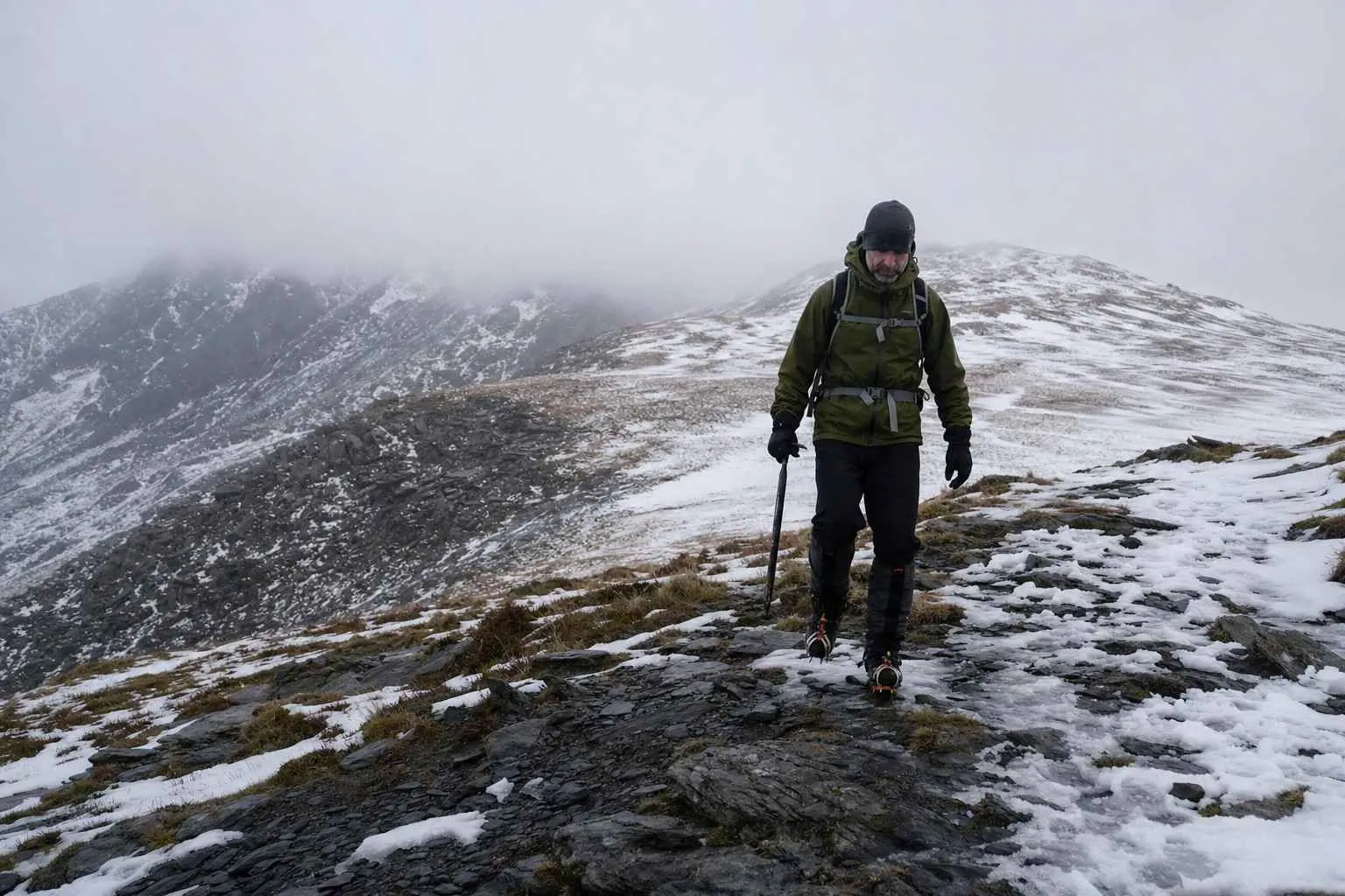 A walker in winter gear on a snow-covered Welsh mountain ridge