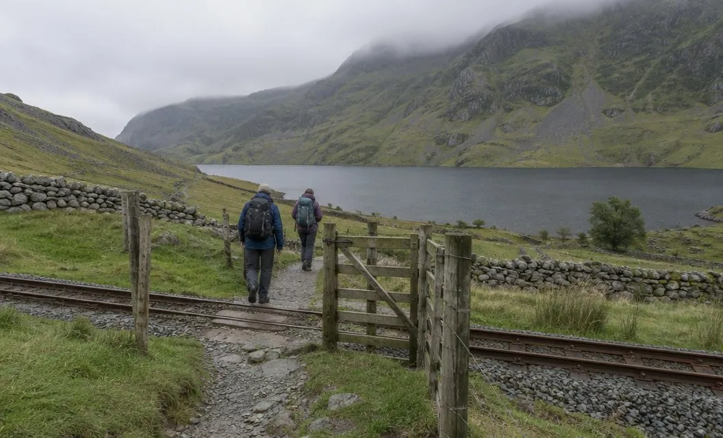 A footpath gate crossing a single narrow-gauge railway line, a lake and hillside behind.
