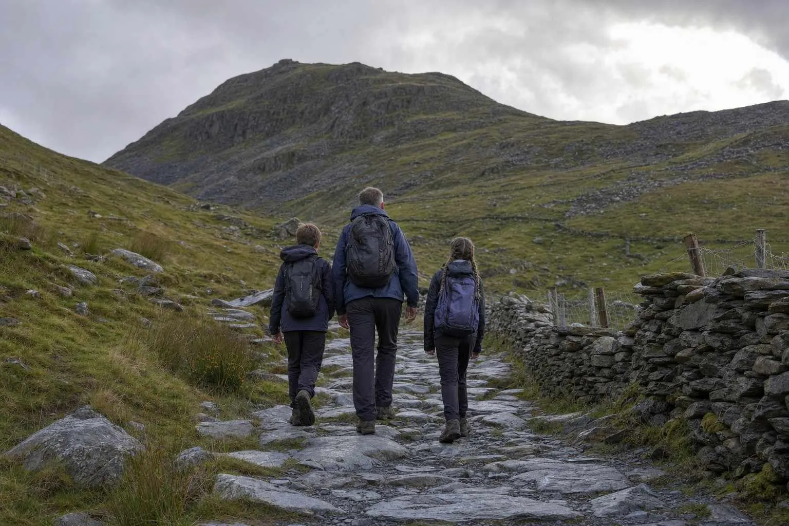 A parent and two children walking up a stony mountain path in waterproofs