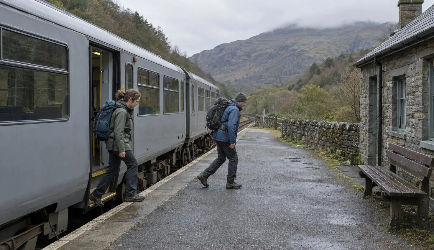 Two walkers with day rucksacks stepping off a short regional train onto a small rural station platform in a wooded valley.