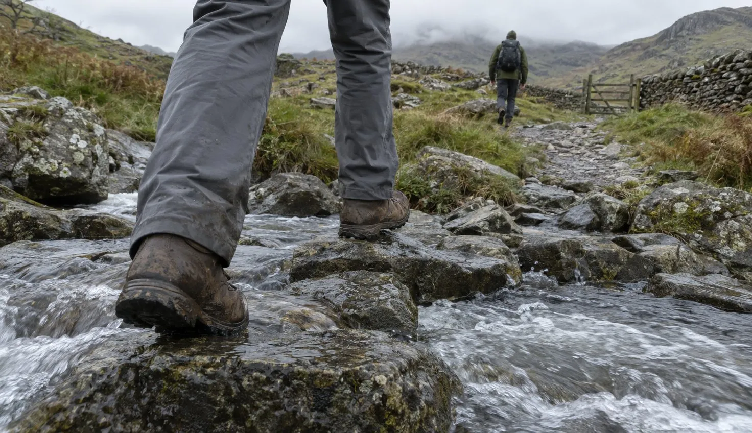Muddy walking boots stepping across wet stones in a fast hill stream.