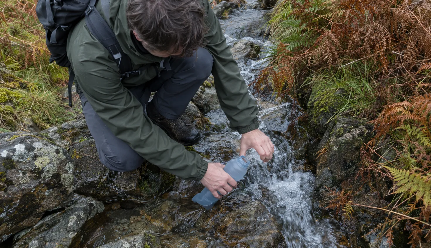 A walker's hands filling a soft bottle in a small fast-running mountain stream.