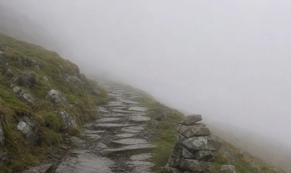 A stony mountain path disappearing into low cloud in Snowdonia