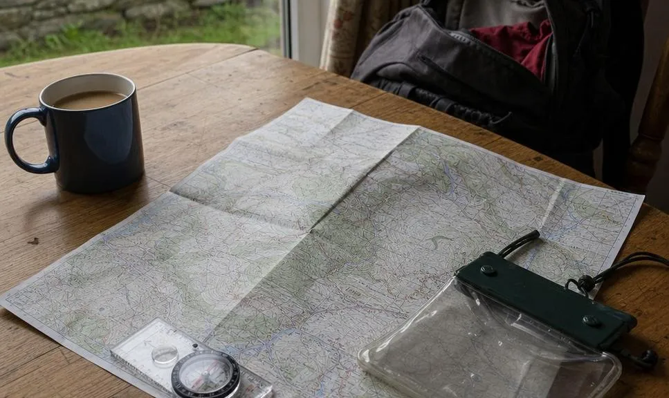 A folded walking map, compass and map case laid out on a kitchen table