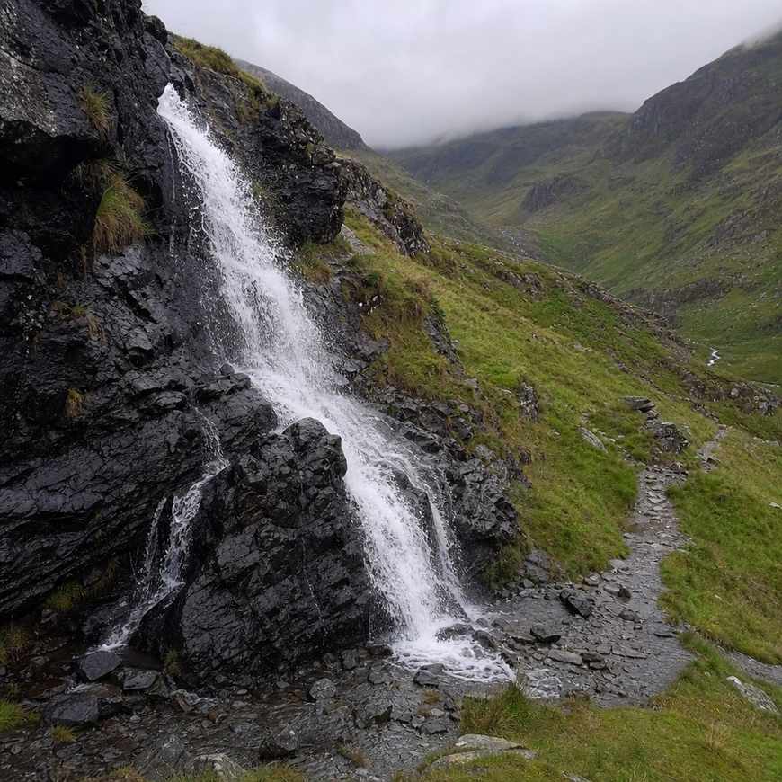 a waterfall over dark rock in a green Welsh valley