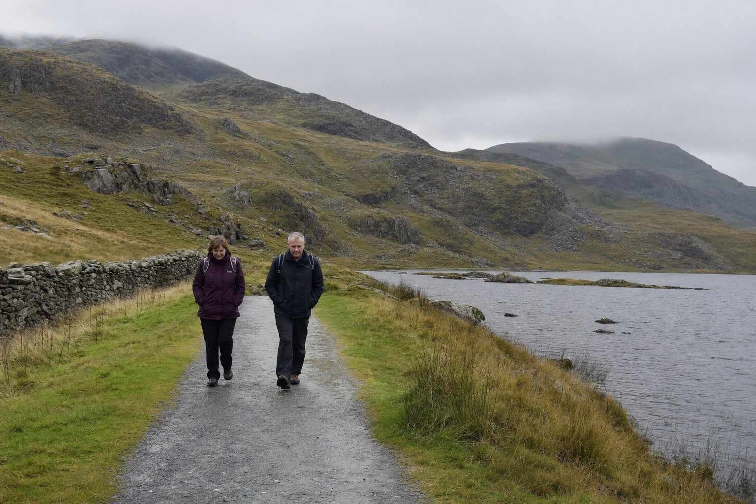two walkers on a gentle path beside a mountain lake