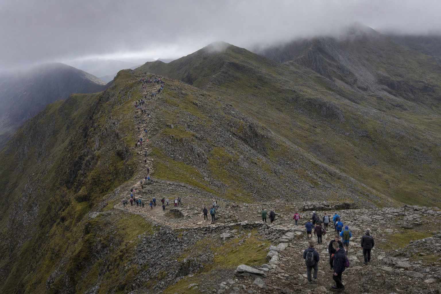 a long line of walkers strung out along a busy stony path high on Snowdon