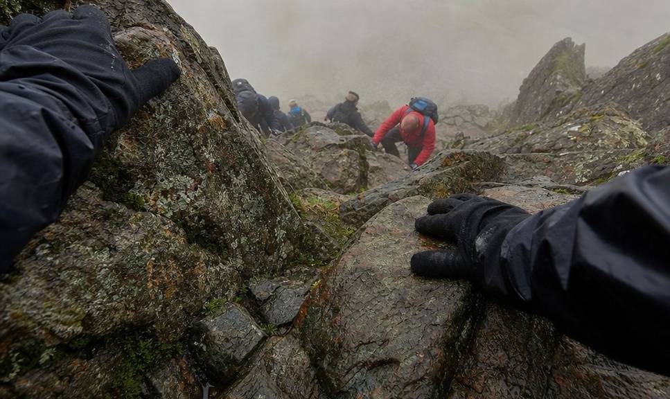 Hands gripping bare rock on a steep scramble in poor weather