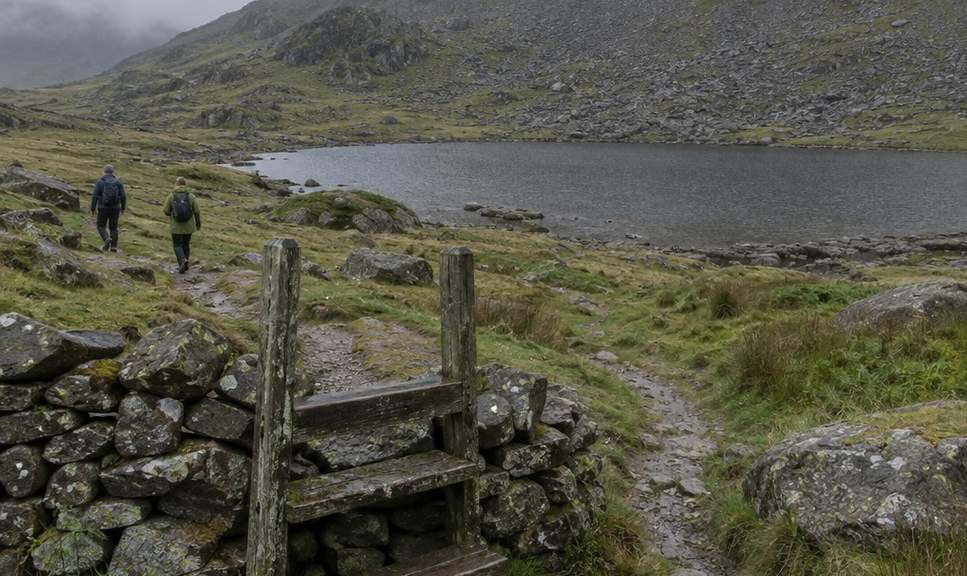 The stile at the top of the Devil's Kitchen path, with Llyn y Cwn beyond and the scree slope to Glyder Fawr rising into cloud.