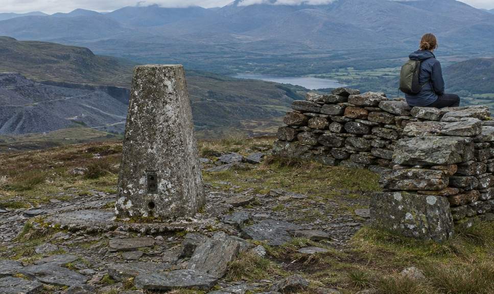 The trig pillar and rough shelter wall on Moel Siabod's summit, looking across to higher peaks with cloud on their tops.
