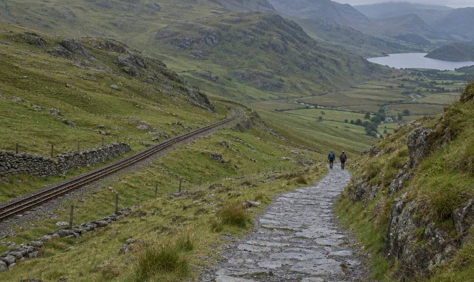 The broad Llanberis Path curving downhill with the mountain railway line running parallel across the slope.